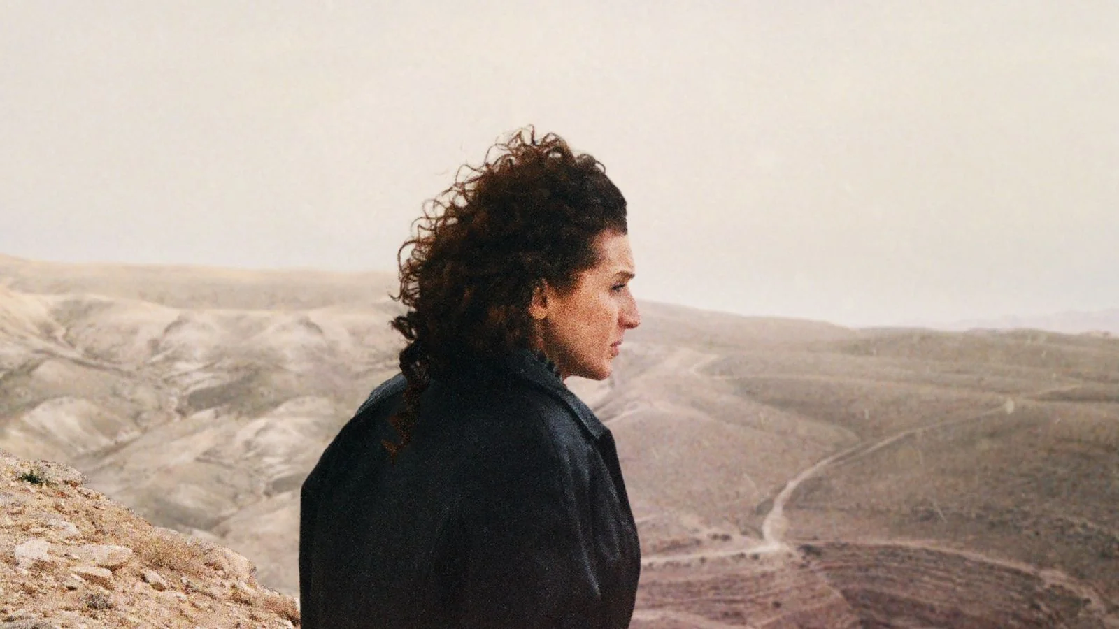 A woman looks across a dry, hilly landscape in House of Hope.