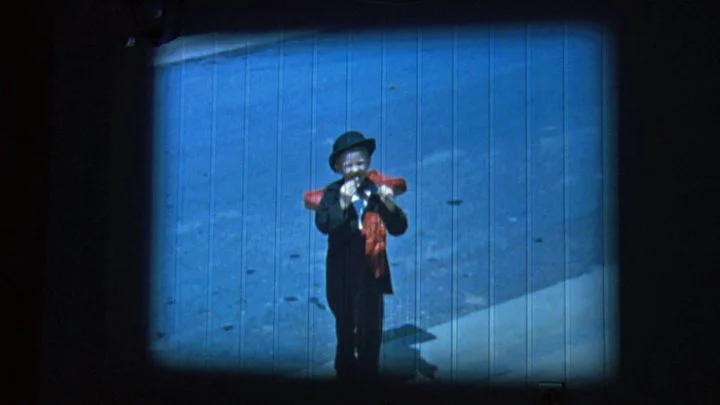A figure stands against a blue background in a projected image from Poule des Doods.